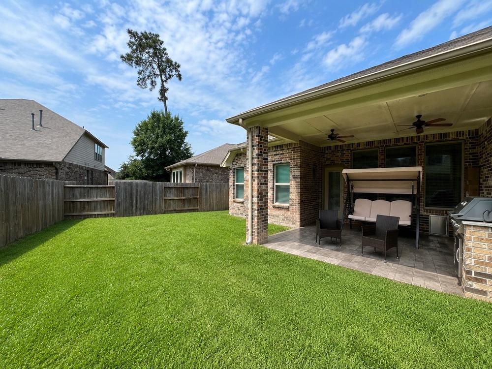 The covered back patio and fenced lawn, with seating and ceiling fans